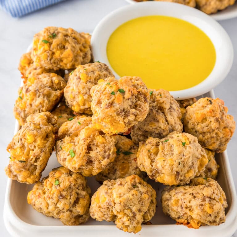 A plate of cheddar bay sausage cheese balls is being served next to a bowl of honey mustard for dipping.