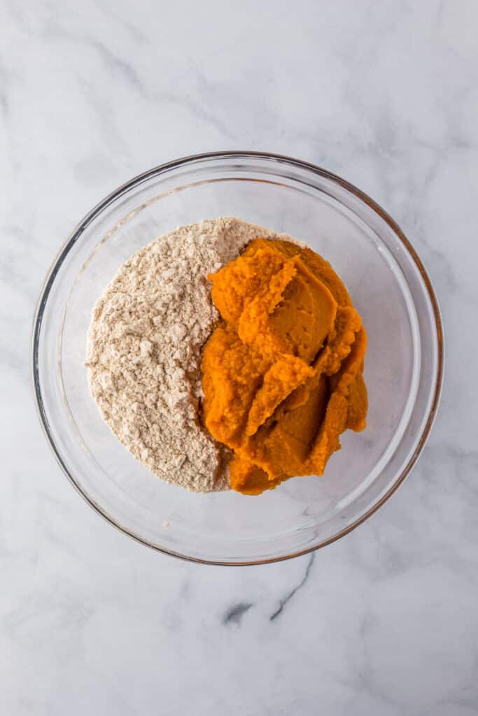 A glass bowl full of pureed pumpkin and spice cake mix before mixing into a pumpkin poke cake batter.
