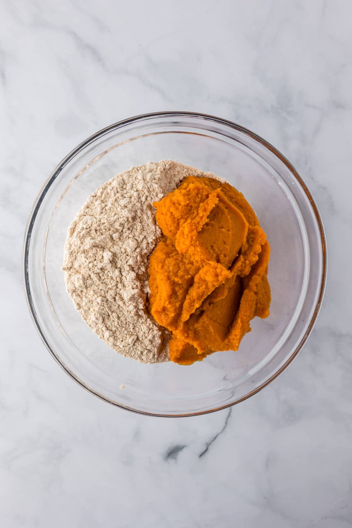 A glass bowl full of pureed pumpkin and spice cake mix before mixing into a pumpkin poke cake batter.