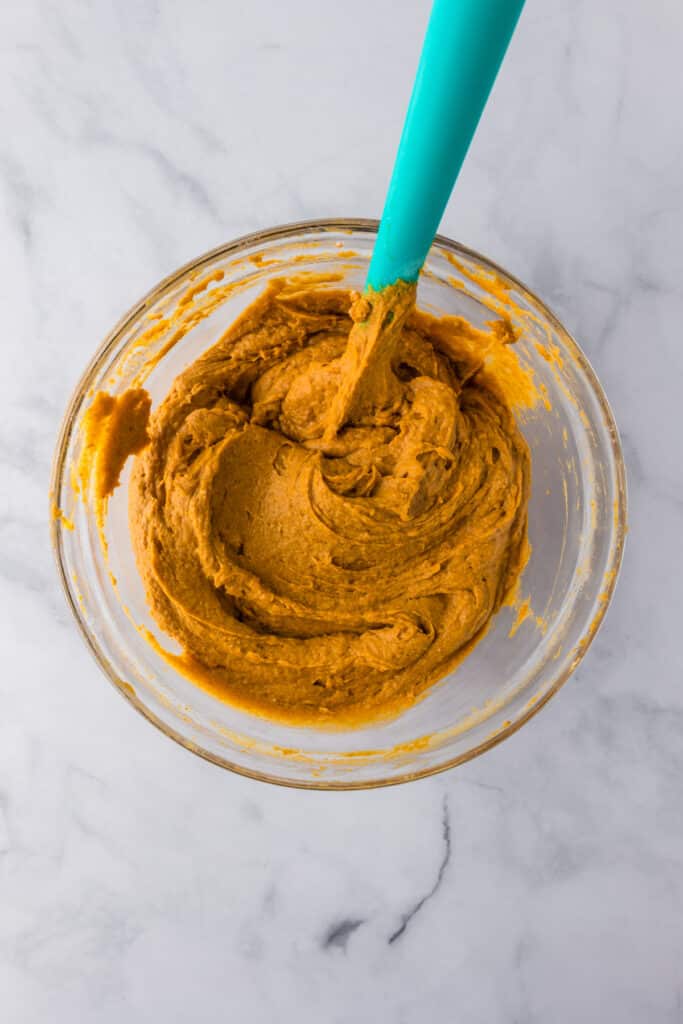 A glass bowl filled with a pumpkin poke cake batter after mixing with a spatula.