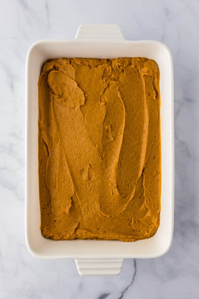 Rectangular baking dish filled with an even layer of raw pumpkin poke cake batter.