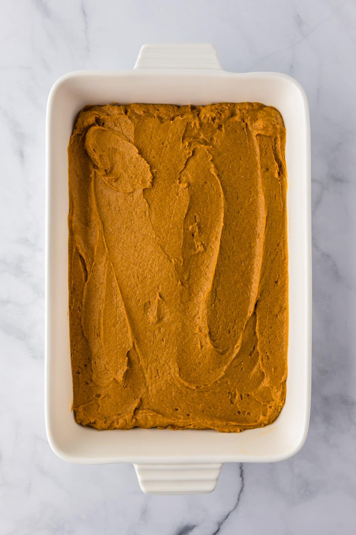 Rectangular baking dish filled with an even layer of raw pumpkin poke cake batter.