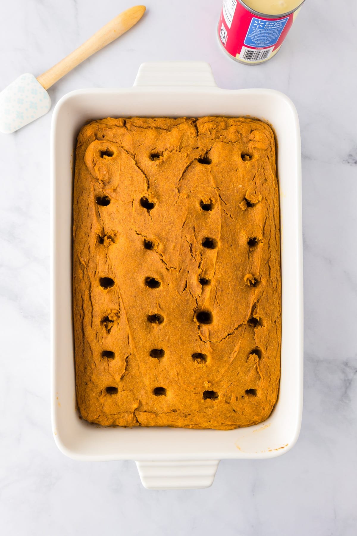 Rectangular baking dish filled with an even layer of baked pumpkin poke cake with rows of holes poked in the cake.