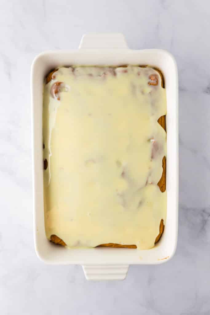 A rectangular baking dish full of a pumpkin poke cake freshly topped with sweetened condensed milk.