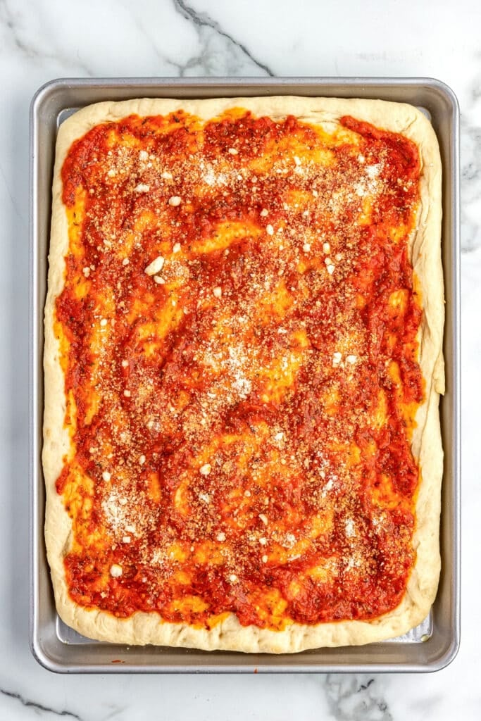Rectangular sheet pan pizza with tomato sauce and grated parmesan cheese on top.