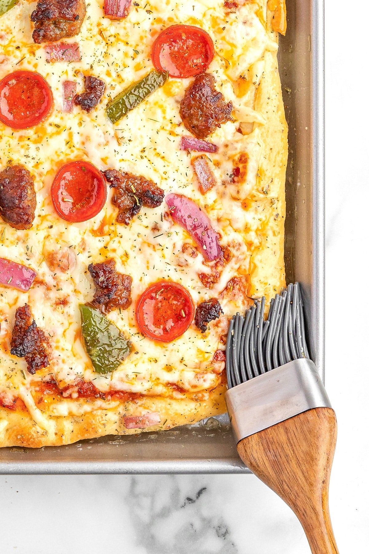 Melted butter being brushed on the crust of baked sheet pan pizza.
