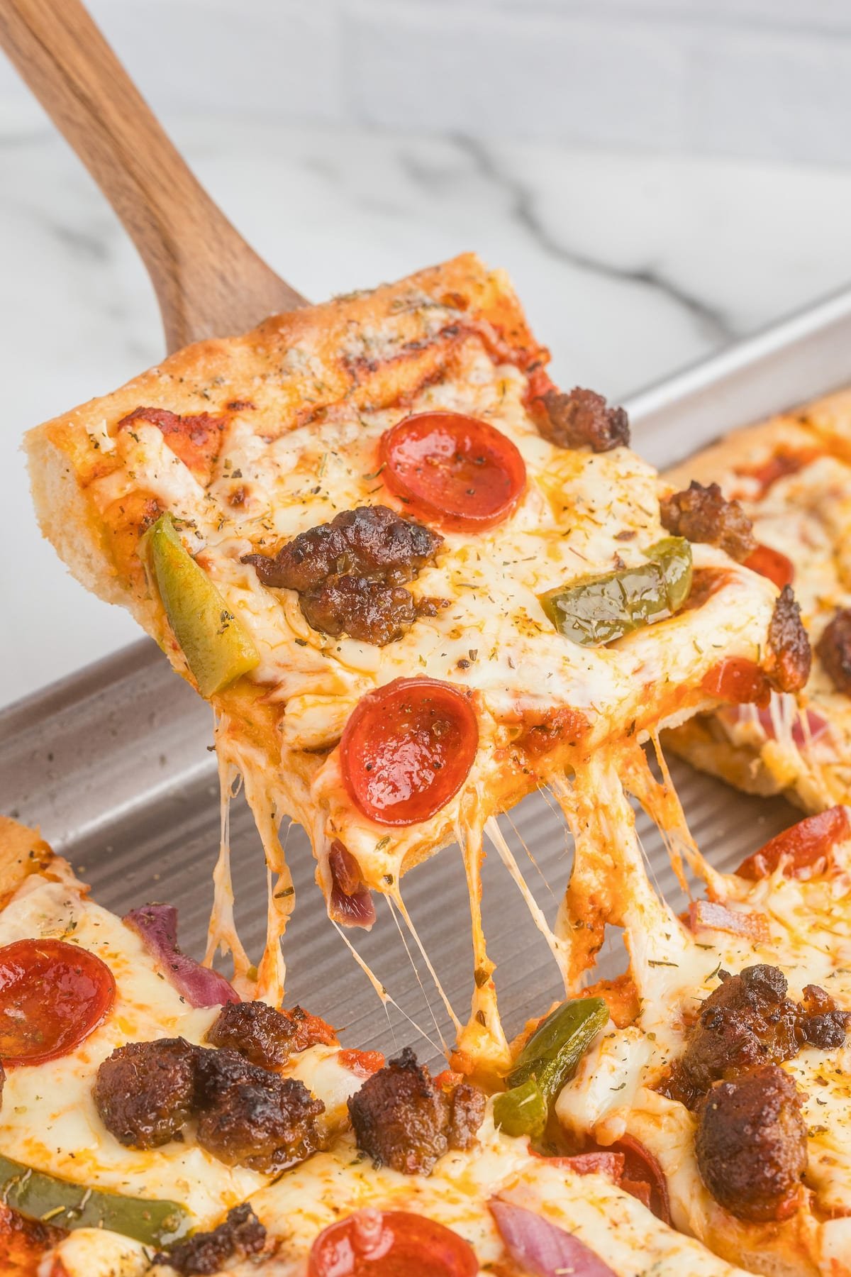 A slice pizza being lifted from the pan with pepperoni, sausage, green bell peppers, and melted cheese.