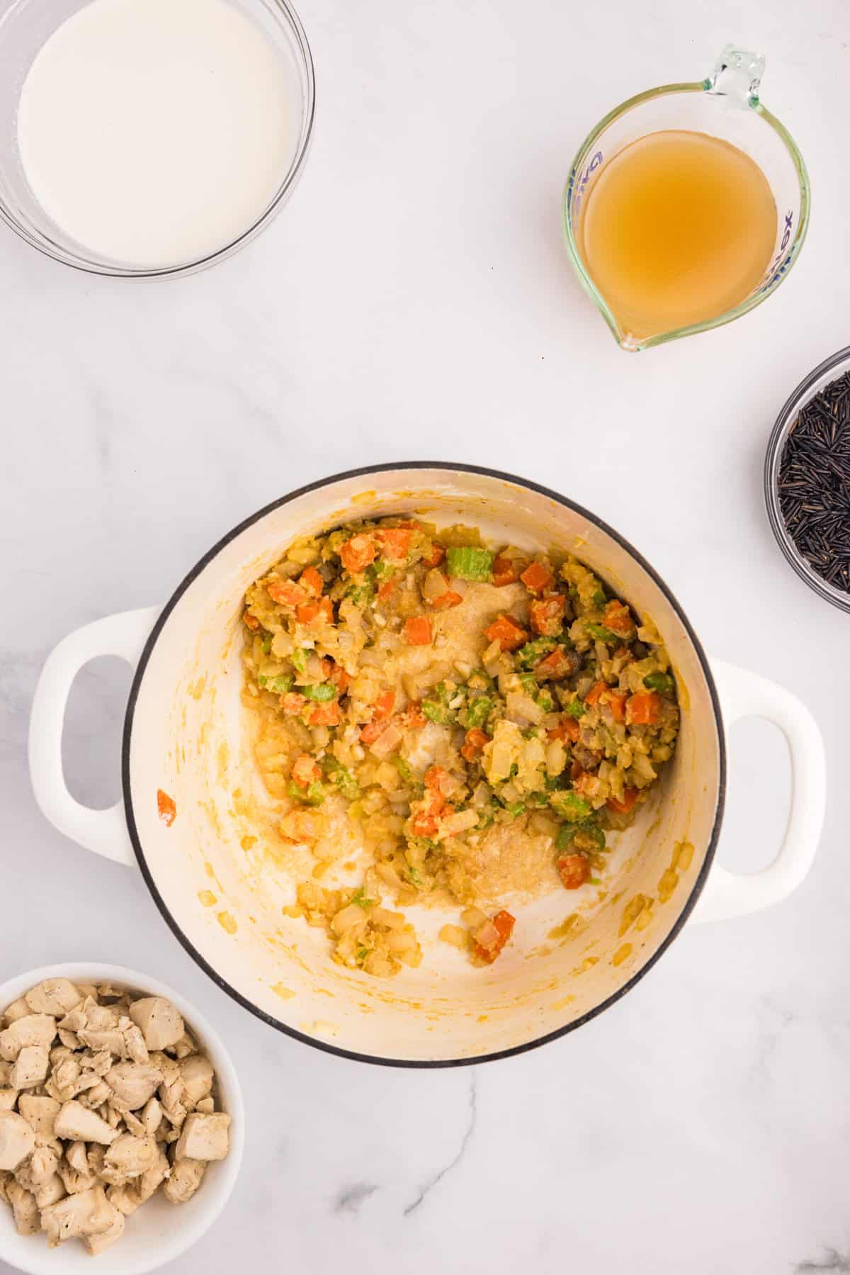 A white pot with sautéed vegetables being cooked with a flour mixture for creamy chicken wild rice soup.