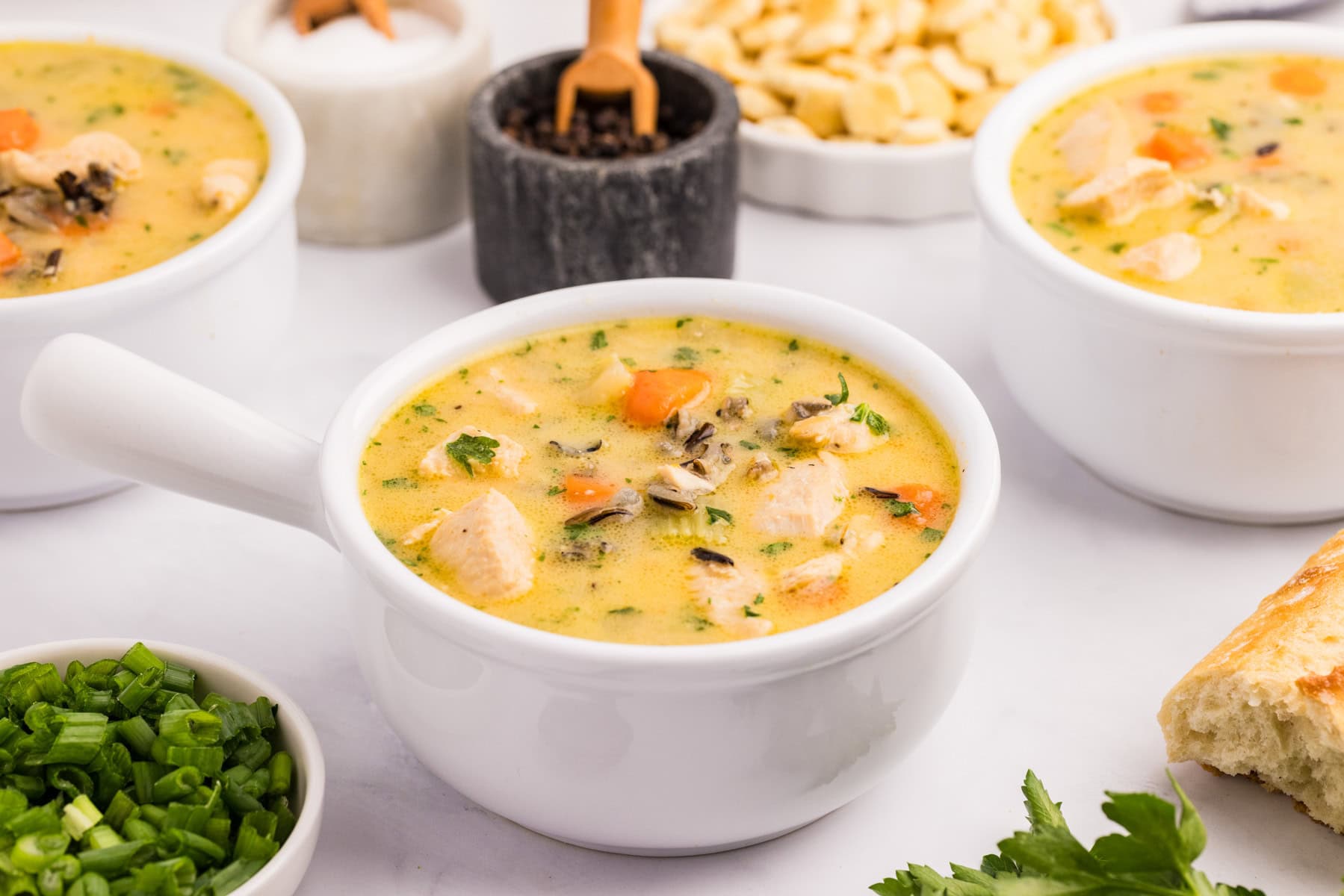 A white bowl filled with creamy chicken and wild rice soup, garnished with chopped herbs with more in the background.