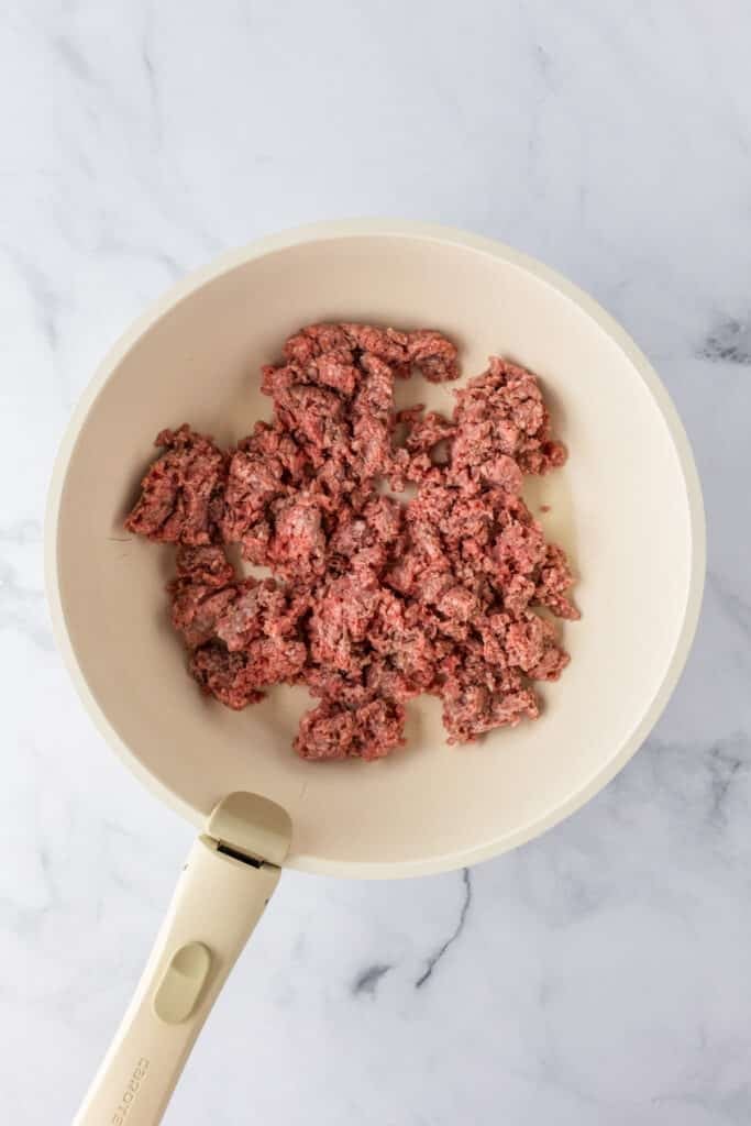 Raw ground beef in a light-colored frying pan for ground beef stroganoff on a counter.