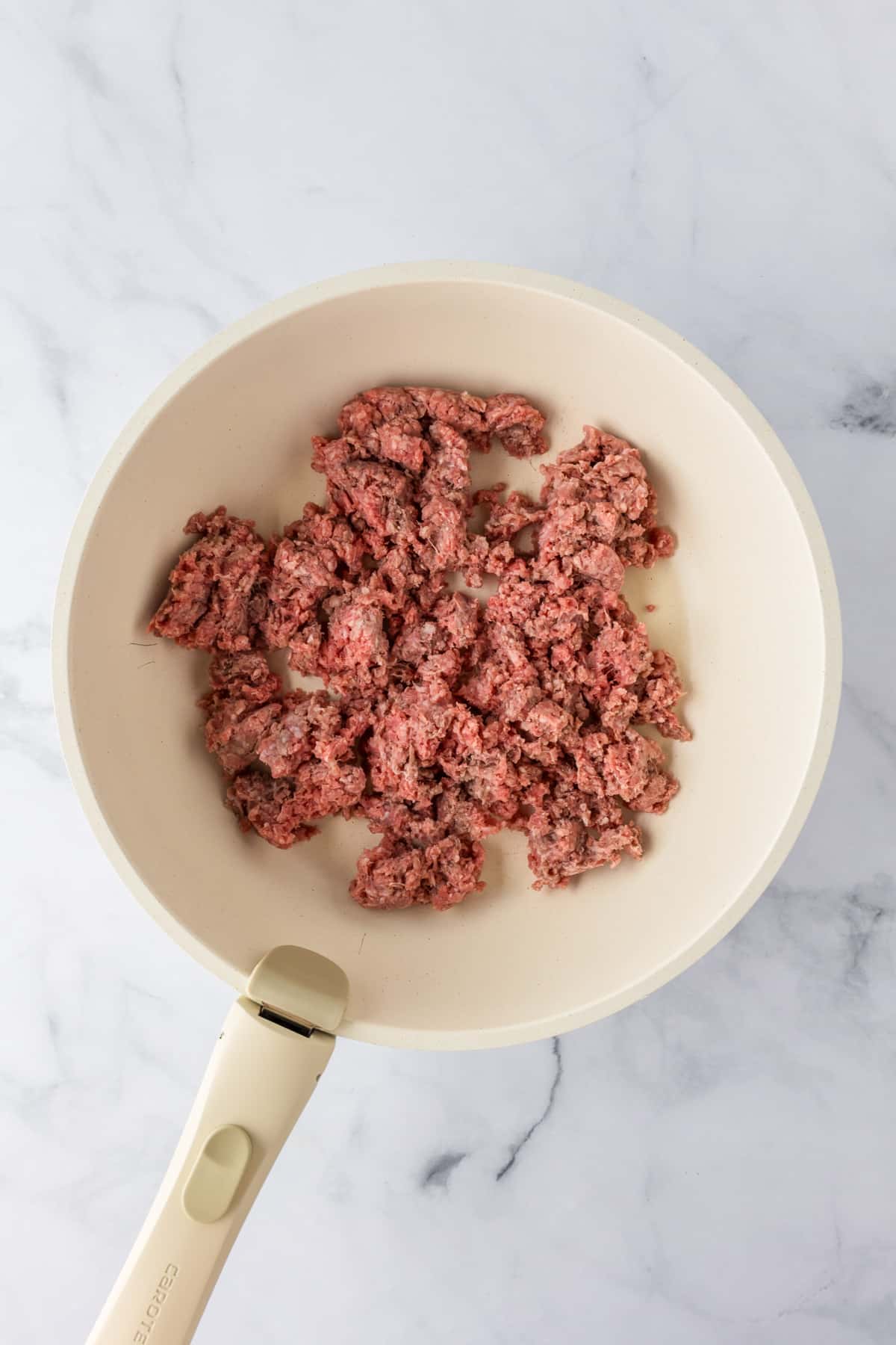 Raw ground beef in a light-colored frying pan for ground beef stroganoff on a counter.