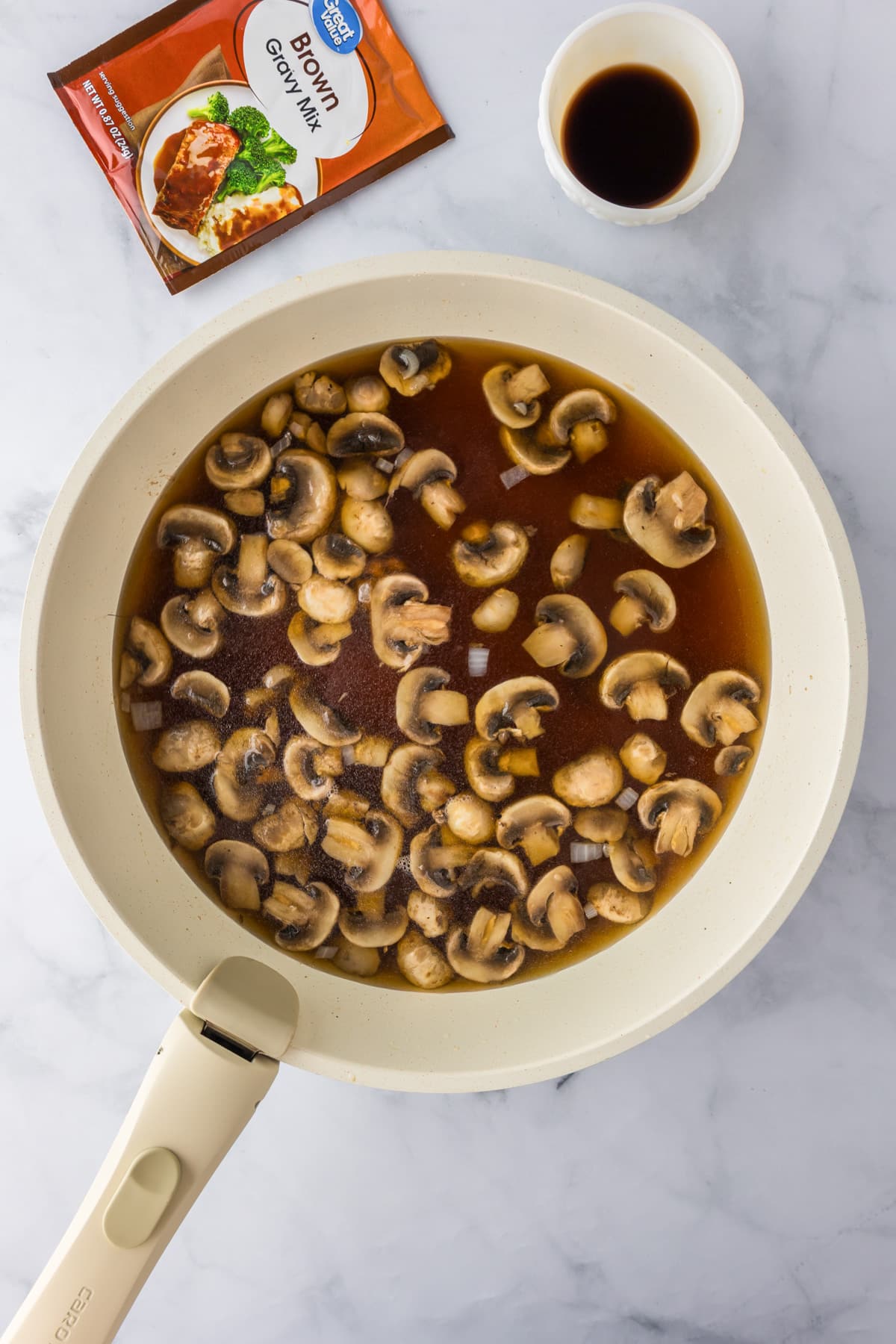 Sliced mushrooms and onions in beef broth for ground beef stroganoff. with a packet of brown gravy mix nearby.