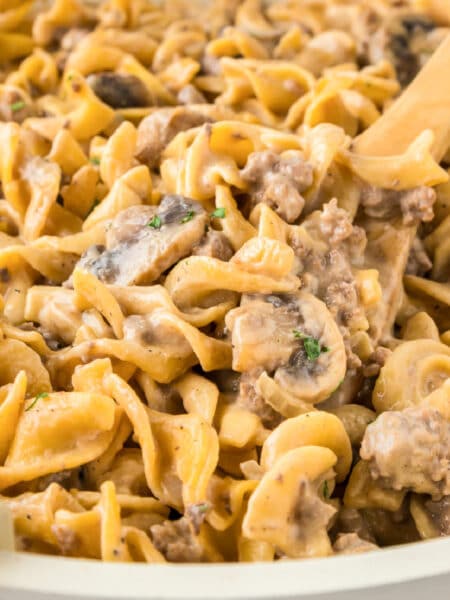 Close-up of creamy ground beef stroganoff with egg noodles, ground beef, mushrooms, and sauce being stirred with a wooden spoon.
