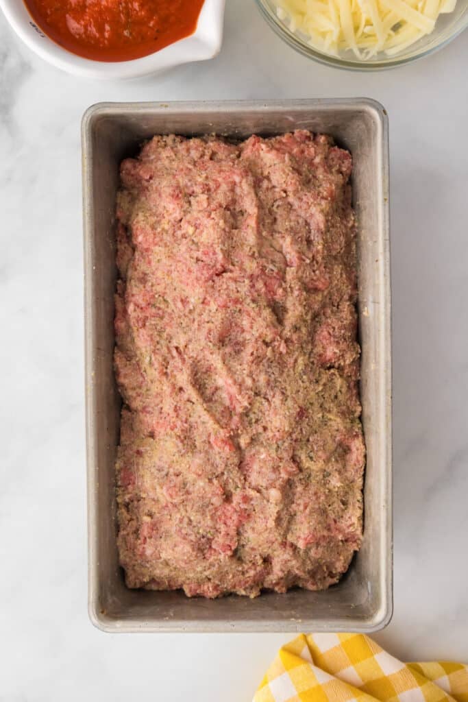 A loaf pan filled with raw Italian meatloaf mixture on a counter.