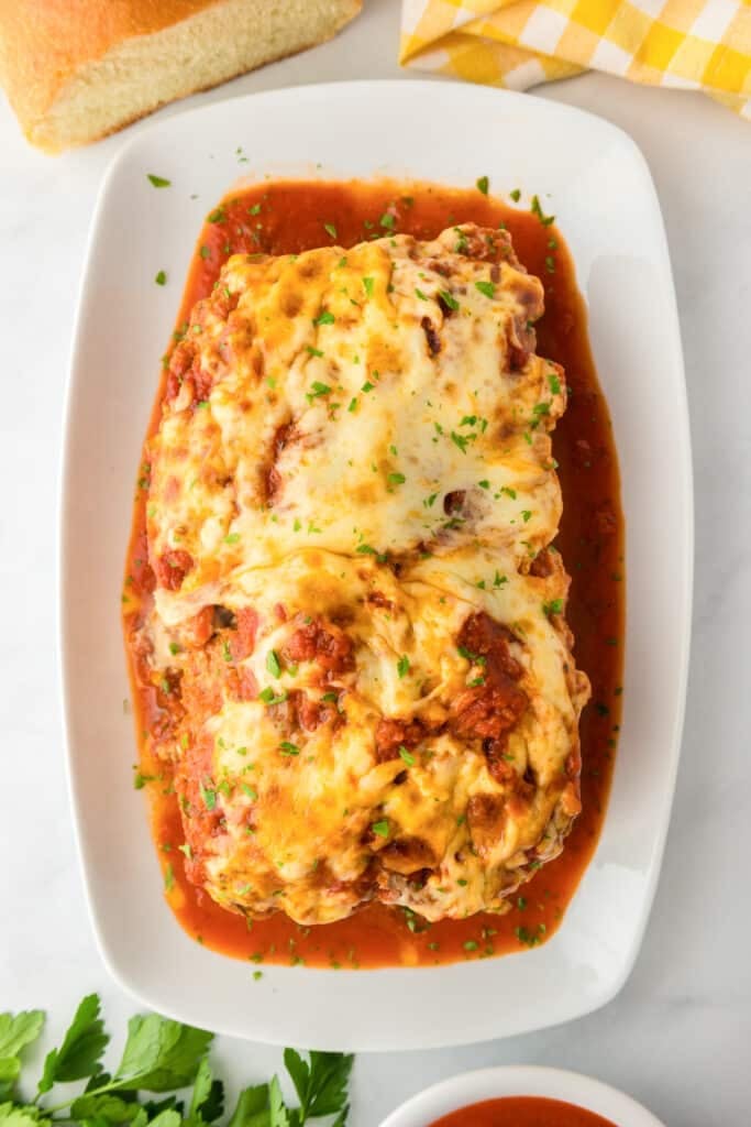 A large platter with a baked Italian meatloaf covered in cheese on a table.