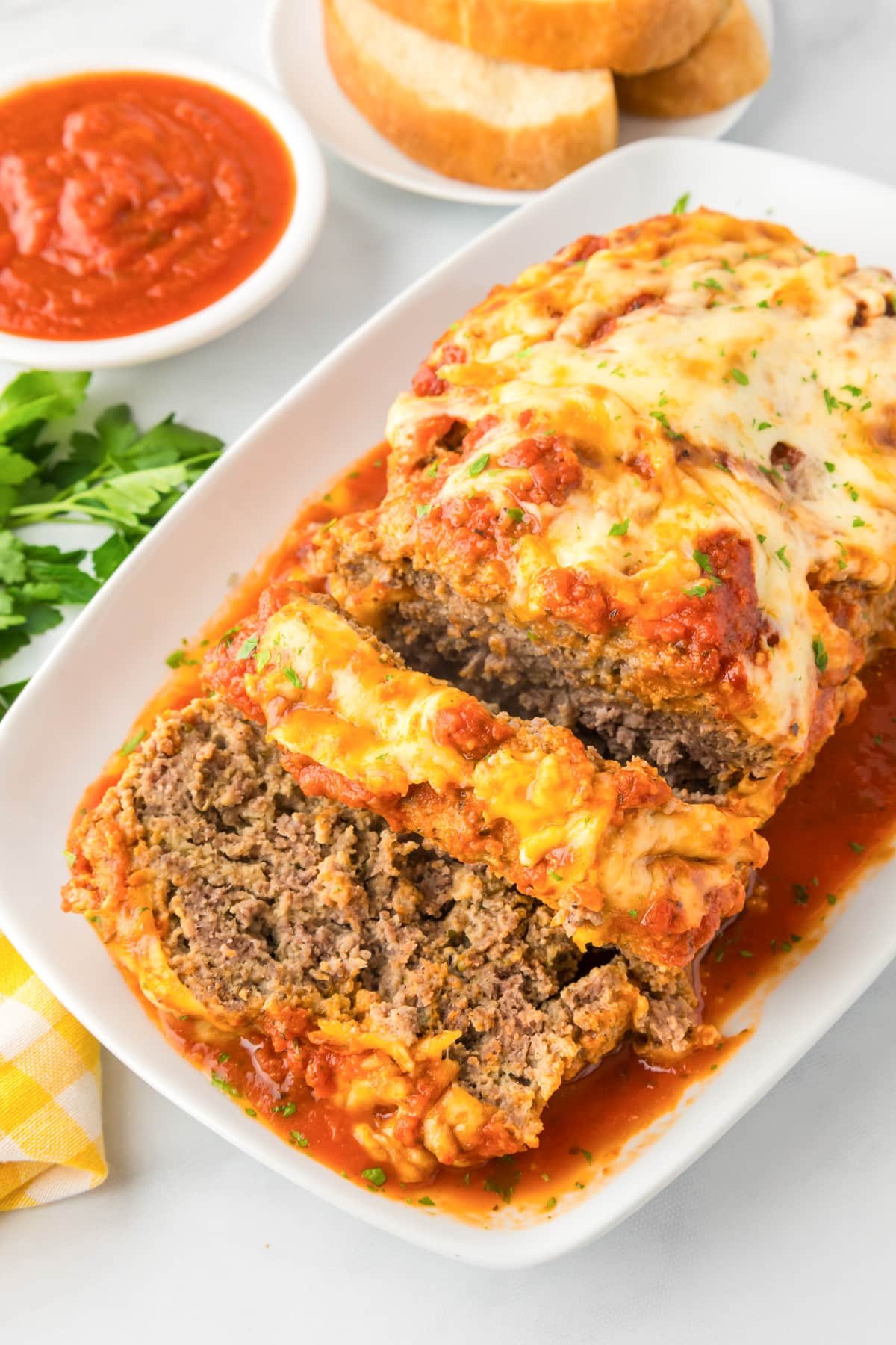 Italian meatloaf topped with marinara and melted mozzarella, sliced on a white platter with garlic bread.
