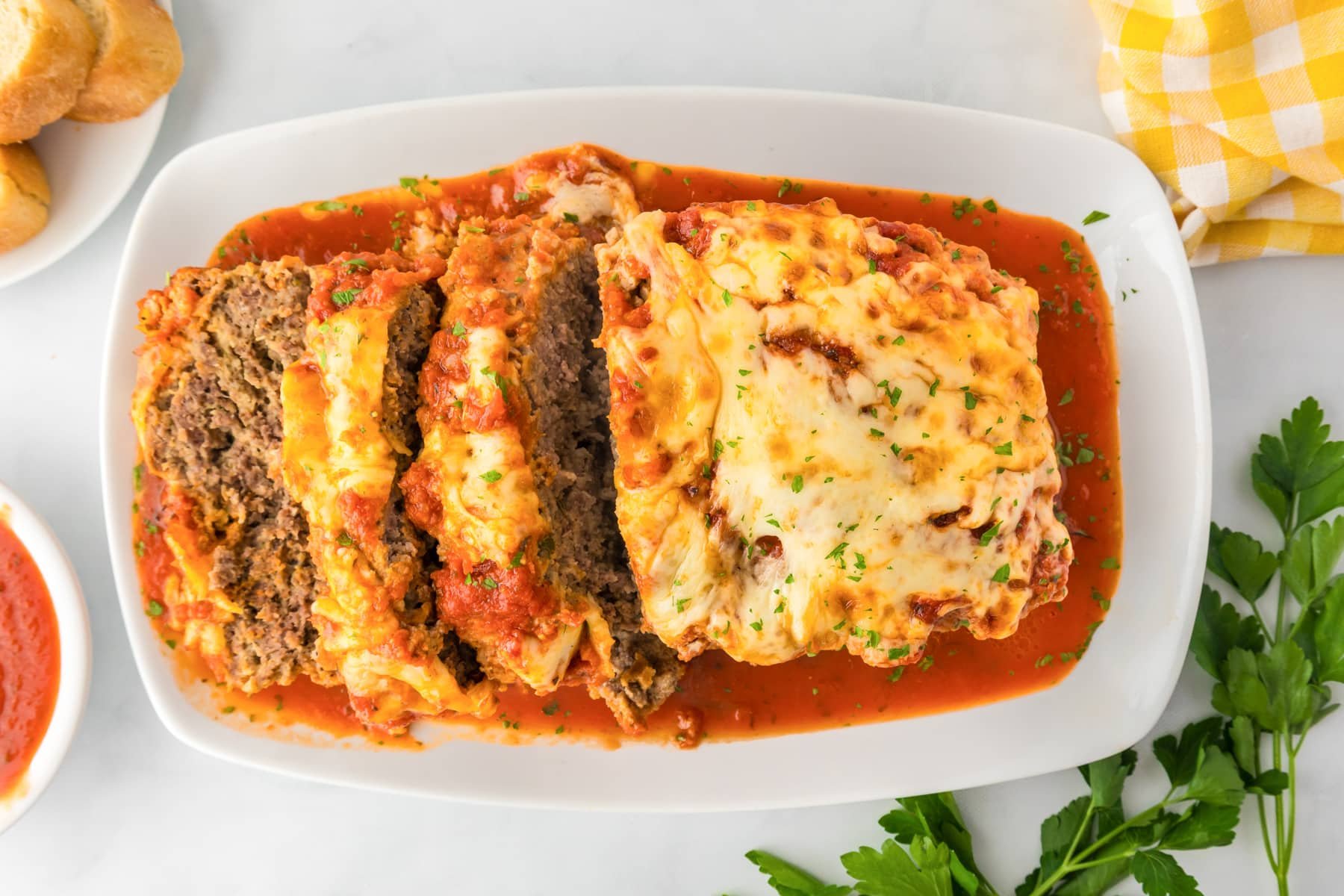 A sliced Italian meatloaf topped with melted cheese and tomato sauce on a platter from above on a table.