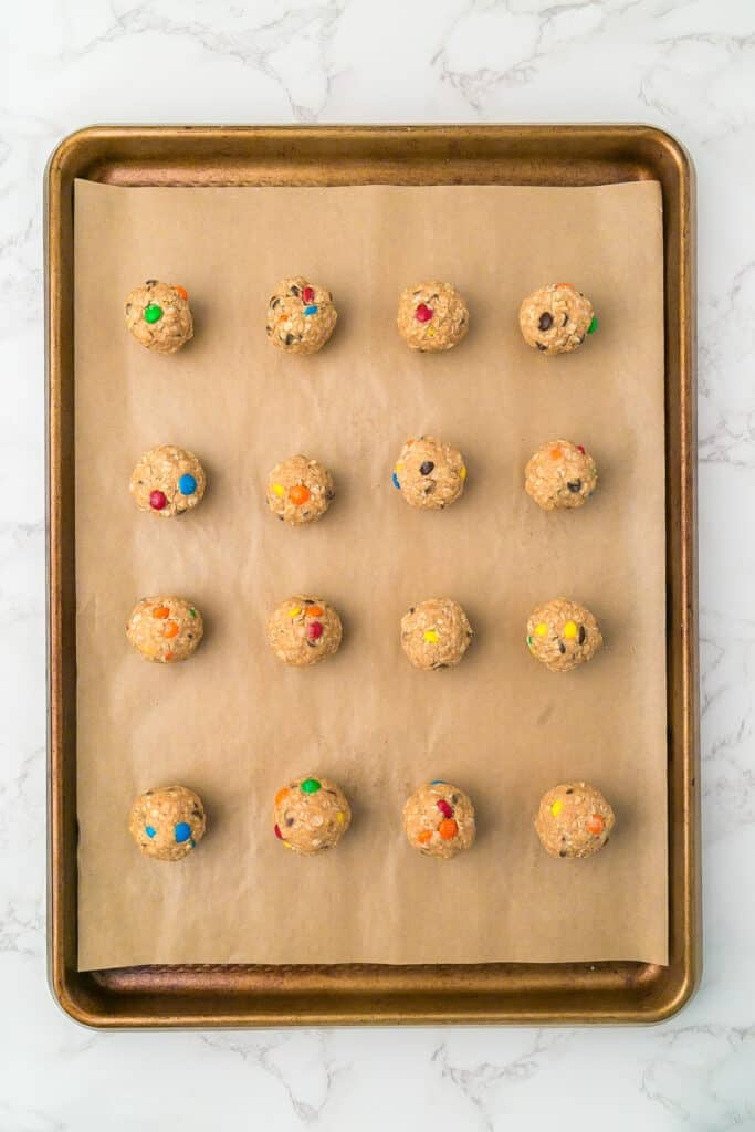 A baking sheet lined with parchment paper full of 16 monster cookie energy balls in rows.