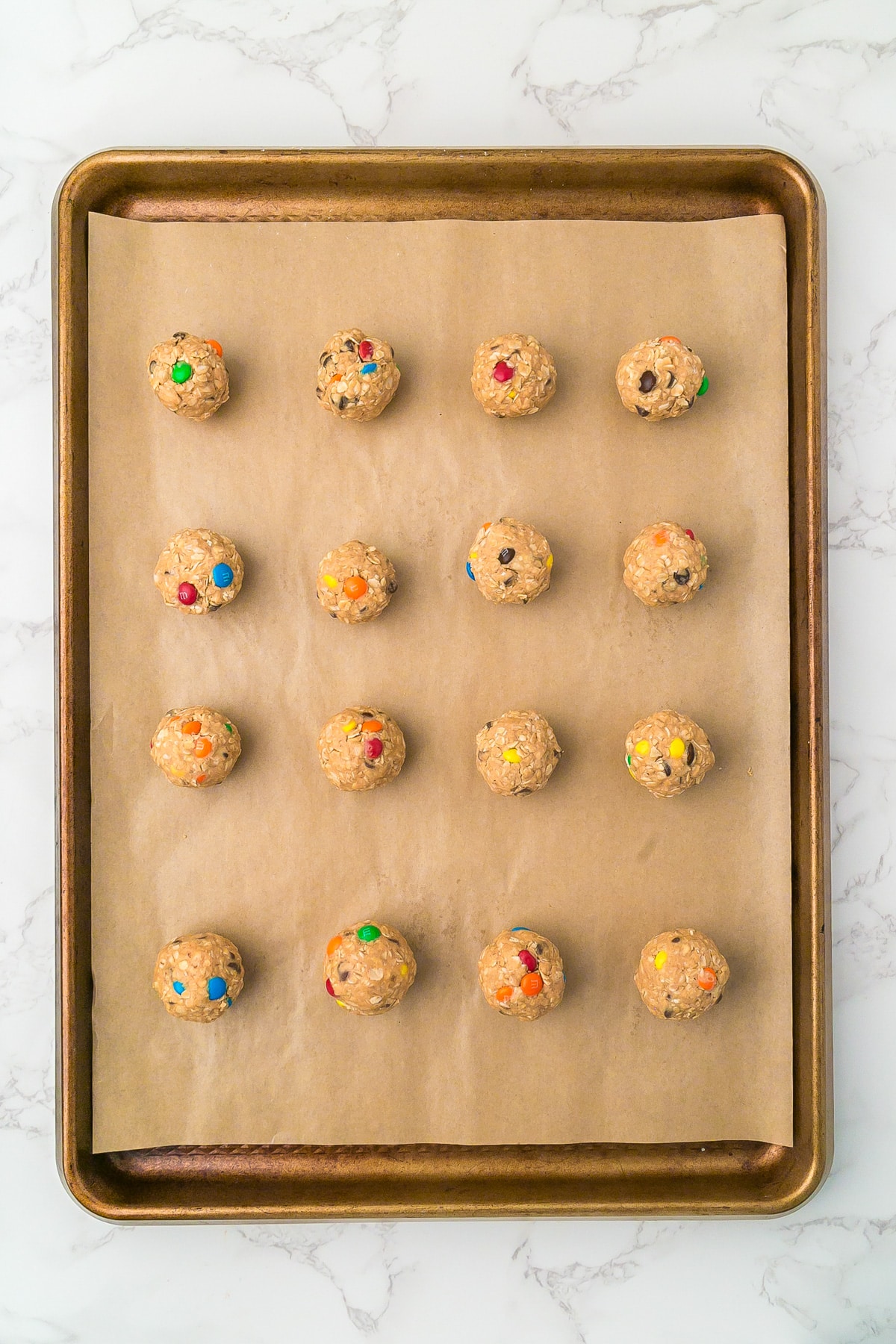 A baking sheet lined with parchment paper full of 16 monster cookie energy balls in rows.