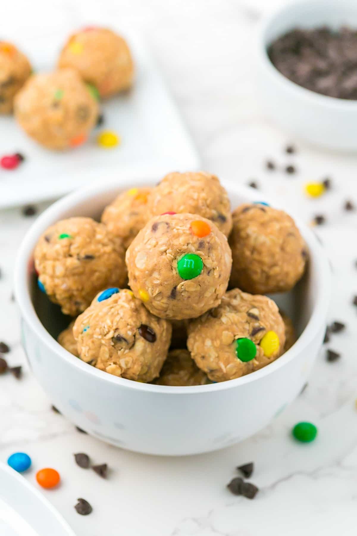A white bowl filled with round Monster cookie energy bites stacked on top of each other with more in the background.