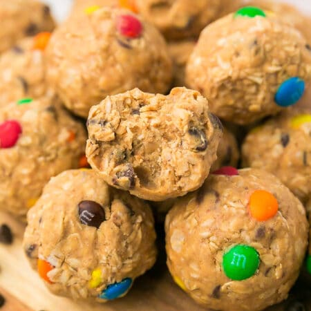 Close-up of oat and peanut butter energy balls with mini chocolate candies, one with a bite taken out, stacked on a wooden surface.