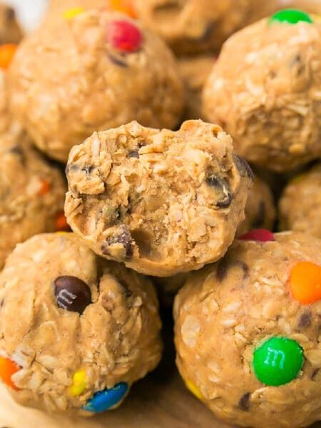 Close-up of oat and peanut butter energy balls with mini chocolate candies, one with a bite taken out, stacked on a wooden surface.