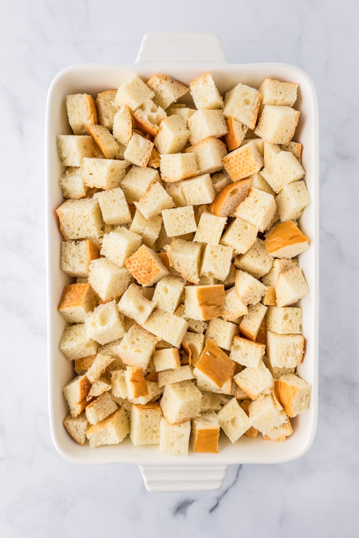 A white baking dish filled with evenly cut cubes of bread, ready to be made into a delicious pumpkin french toast casserole.