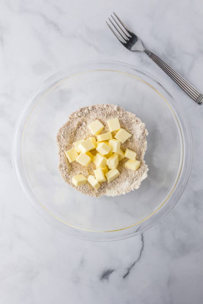 A glass bowl containing flour and cubes of butter sits on a marble surface, with a fork placed above the bowl ready for making a delicious pumpkin french toast casserole crumble topping.