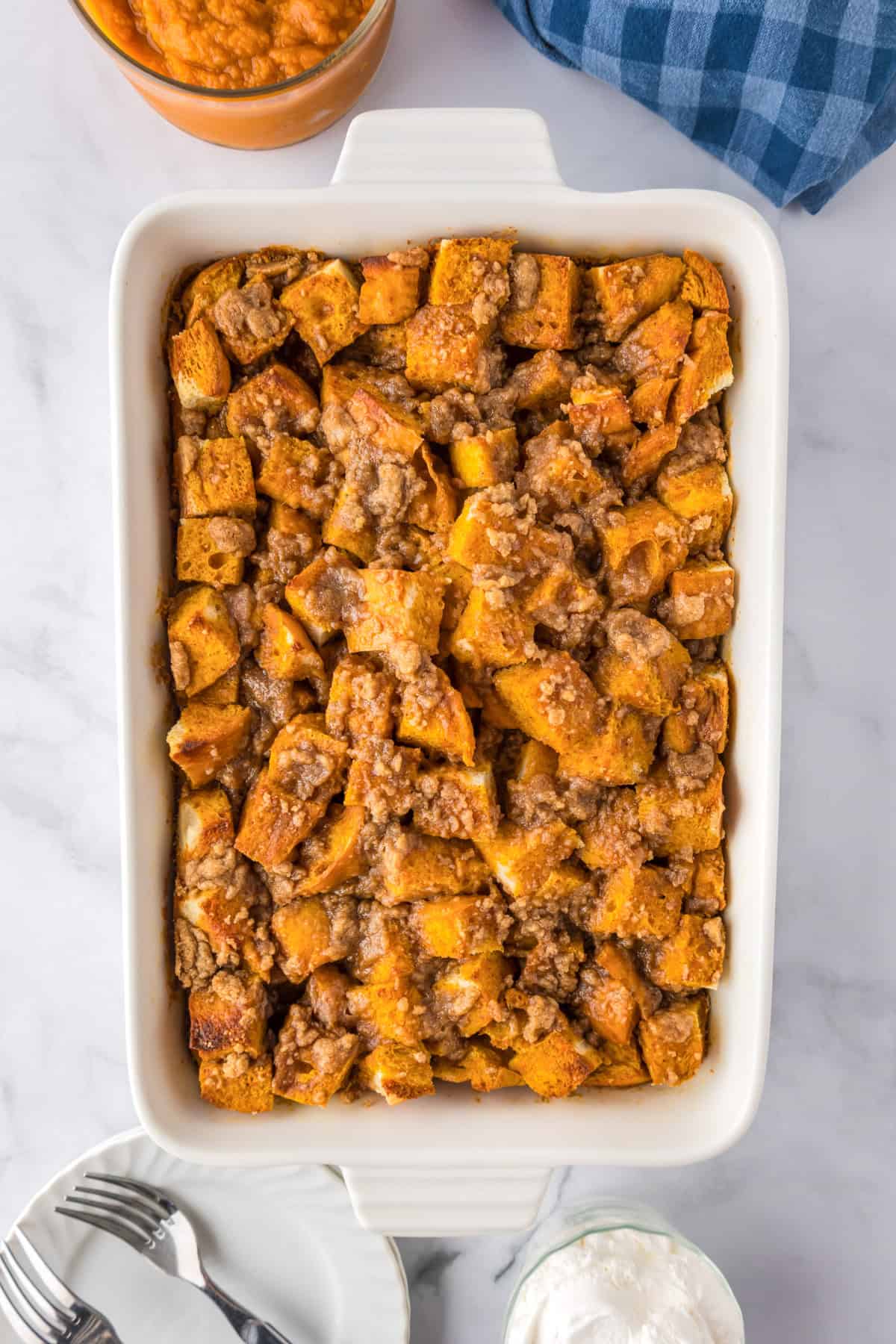 A white rectangular baking dish filled with golden brown cubed bread topped with a crumbly brown streusel for a delicious pumpkin french toast casserole after baking.