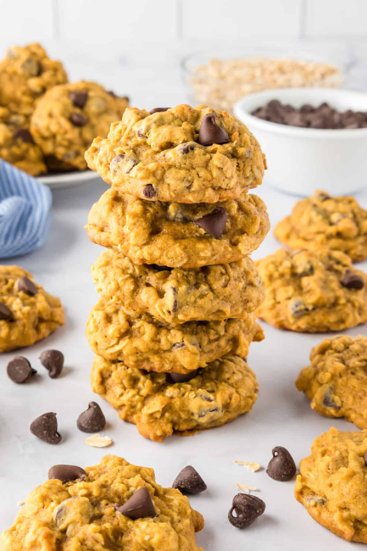 A stack of five pumpkin oatmeal cookies with chocolate chips is surrounded by more cookies nearby on the counter.