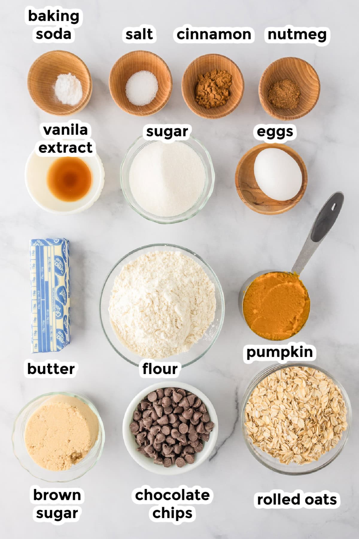 Ingredients for pumpkin oatmeal cookies in bowls on a counter with text labels.