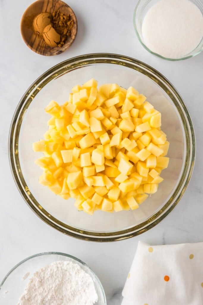 A bowl of diced yellow fruit, perfect as a topping for an apple dessert pizza.