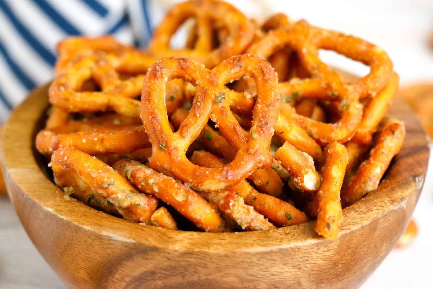 A wooden bowl filled with seasoned ranch pretzel twists, with a blue and white striped cloth in the background.