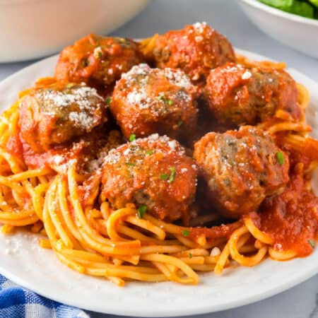 A plate of spaghetti topped with tomato sauce and several ground turkey meatballs, garnished with grated cheese and herbs.