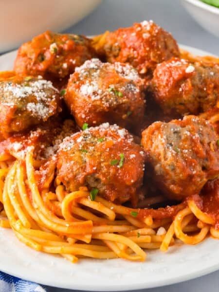A plate of spaghetti topped with tomato sauce and several ground turkey meatballs, garnished with grated cheese and herbs.