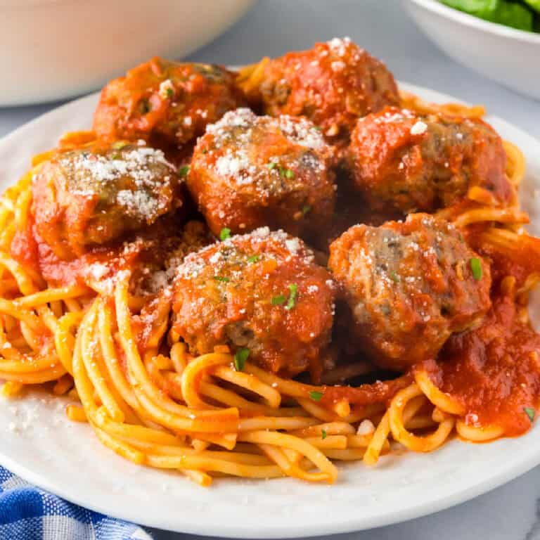 A plate of spaghetti topped with tomato sauce and several ground turkey meatballs, garnished with grated cheese and herbs.