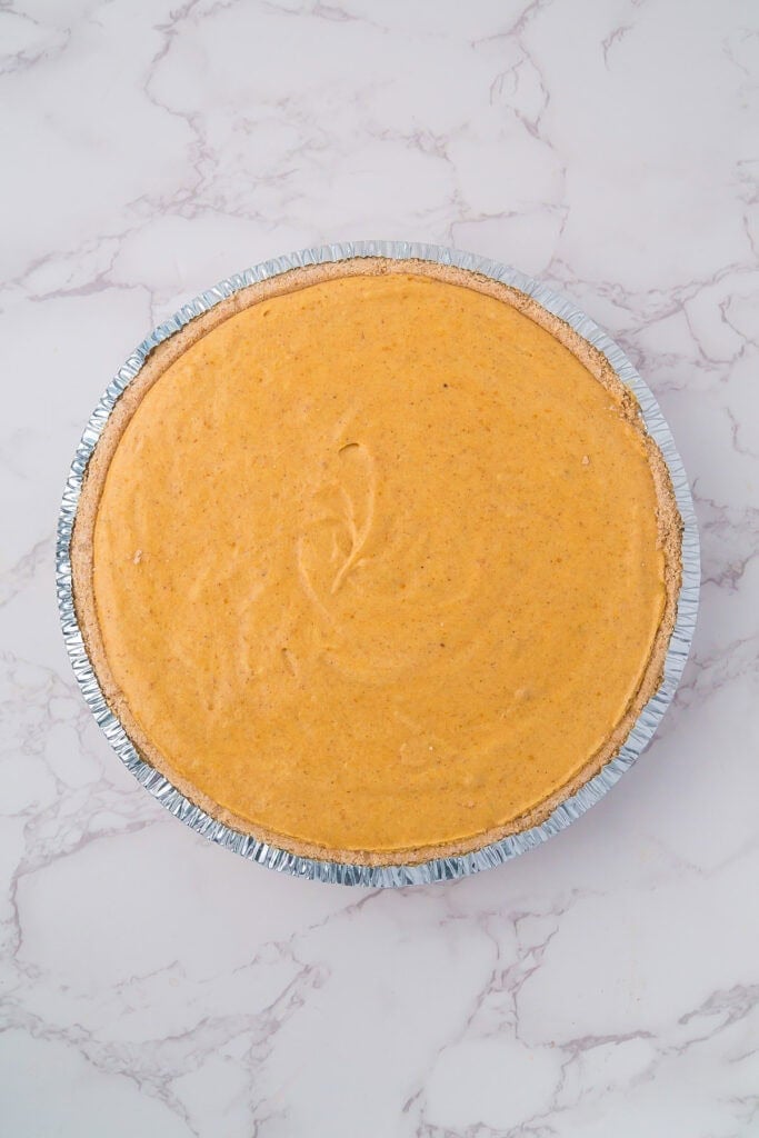 A whole pumpkin marshmallow pie with a graham cracker crust in a foil pie pan after chilling.