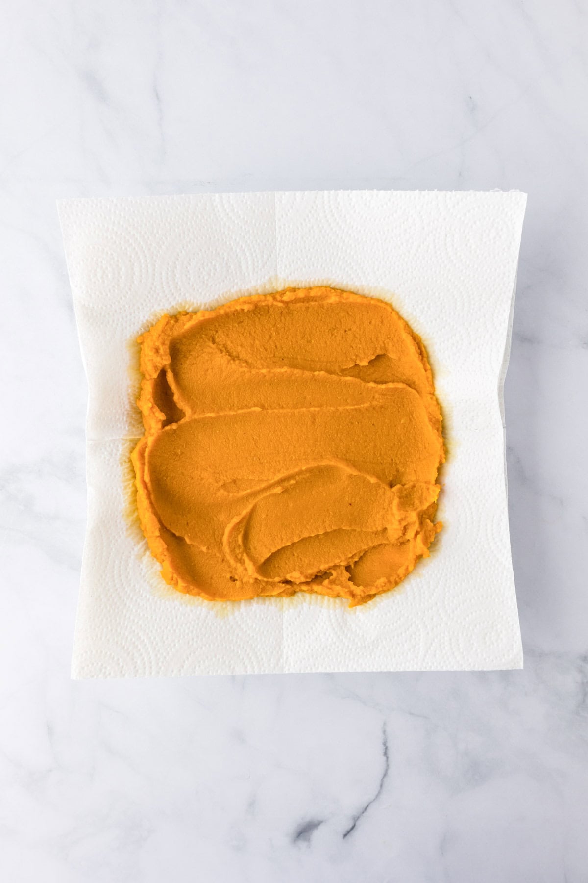 A layer of orange pumpkin puree being blotted on paper towels to remove excess moisture for pumpkin chocolate chip bars.