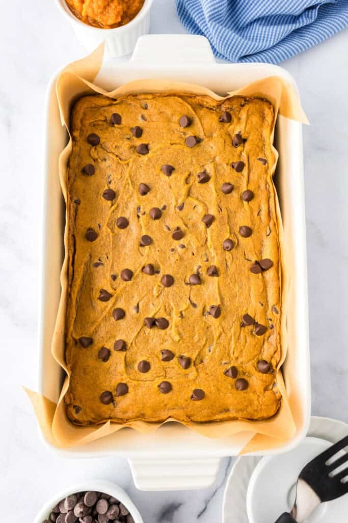 A rectangular baking dish lined with parchment paper full of baked pumpkin chocolate chip bars.