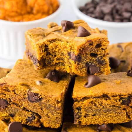 Three pumpkin chocolate chip bars are stacked on top of each other on a platter, with chocolate chips visible inside and a bite missing from the top bar.