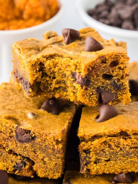Three pumpkin chocolate chip bars are stacked on top of each other on a platter, with chocolate chips visible inside and a bite missing from the top bar.