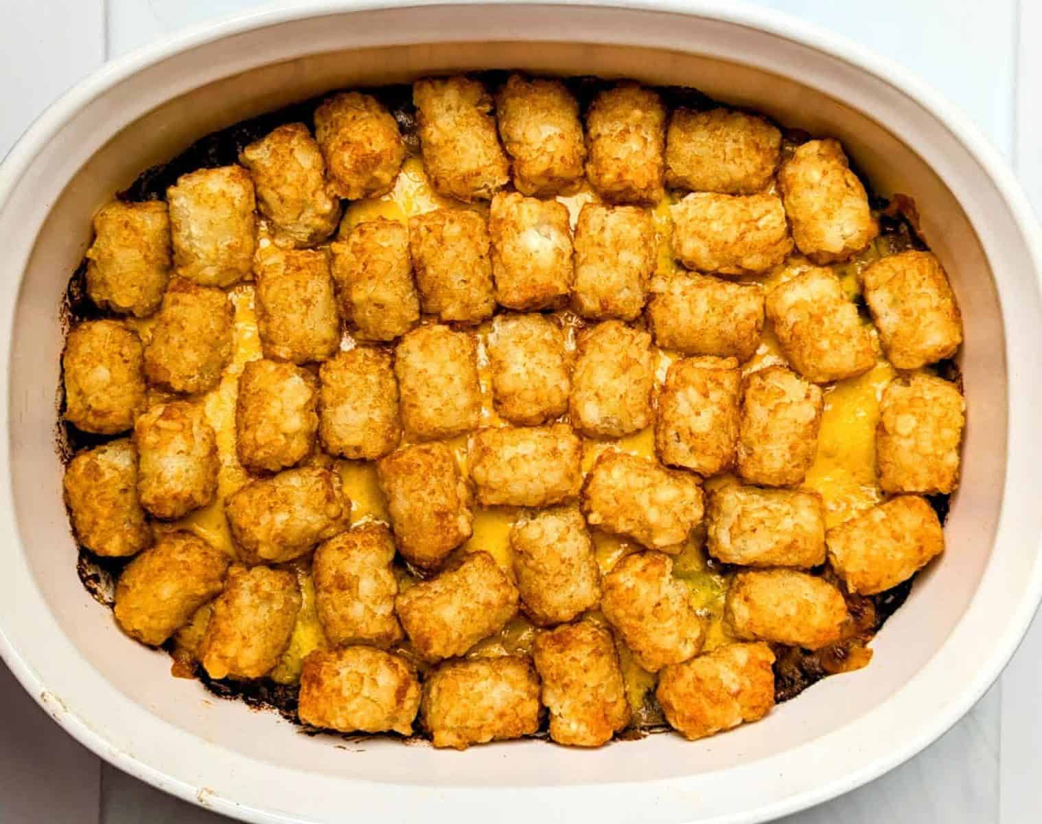 A casserole dish filled with baked tater tots layered over melted cheese and a cooked beef and cheese filling to make big mac casserole