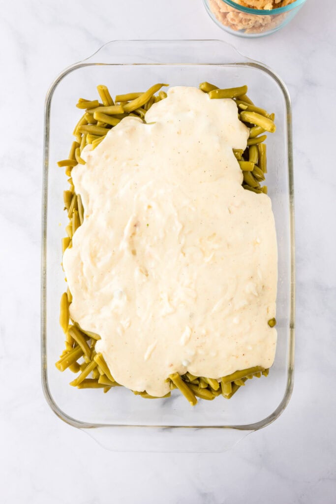 A glass baking dish filled with green bean casserole, featuring tender green beans topped with a layer of creamy white sauce.