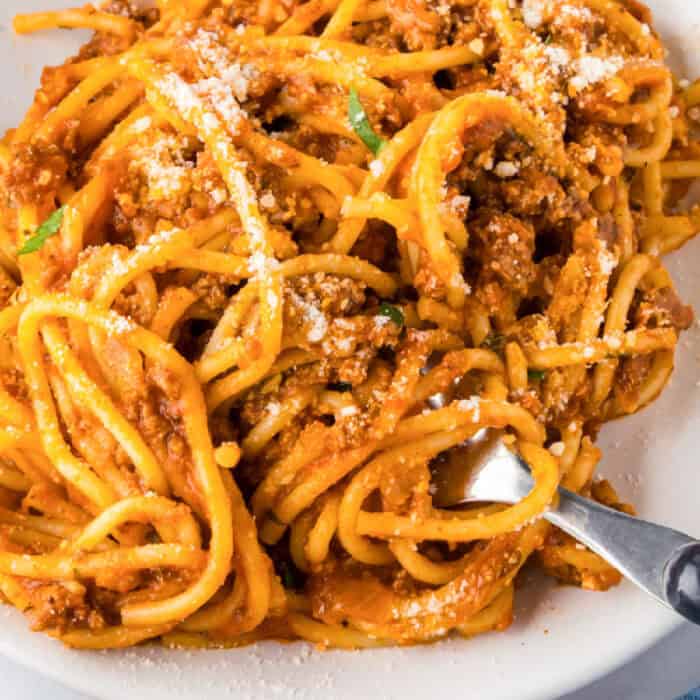 A close-up of ground turkey spaghetti with meat sauce, topped with grated cheese, served on a white plate with a fork twirling noodles.