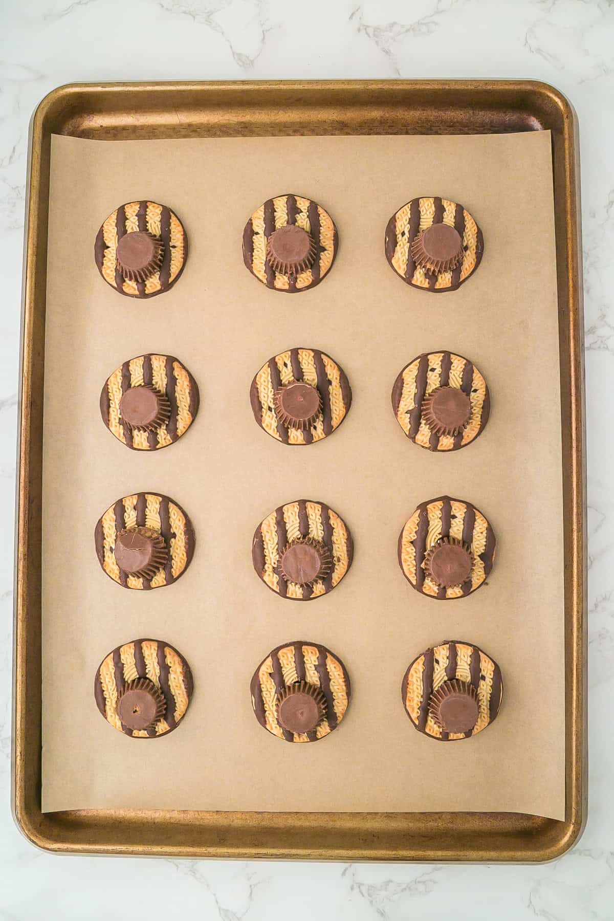 A baking sheet with twelve turkey cookies topped with striped chocolate and a chocolate candy center, arranged in three rows on parchment paper.