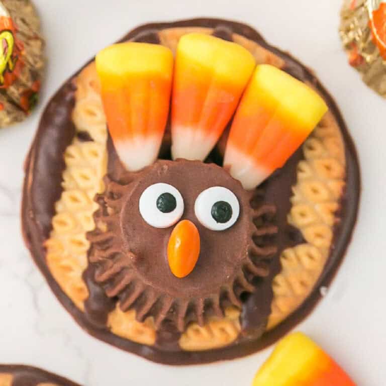 A turkey cookie decorated with a peanut butter cup, candy eyes, an orange candy beak, and three candy corn pieces as colorful feathers.