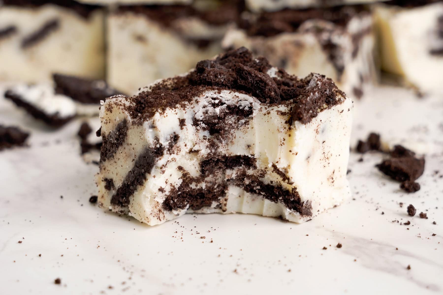 A close-up of a square piece of Oreo fudge with visible cookie crumbs and chunks on a white surface.