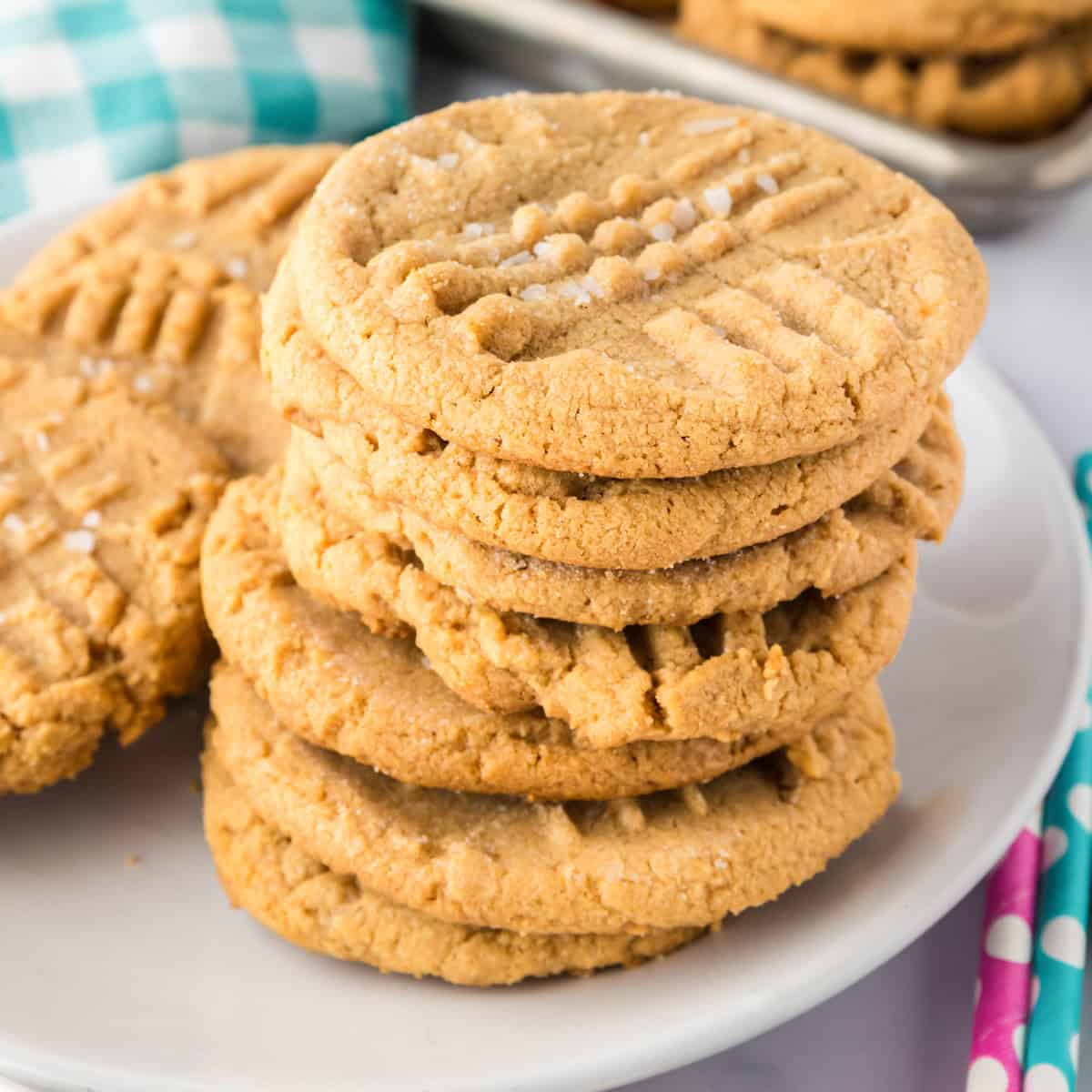 A stack of classic 3 ingredient peanut butter cookies with a crisscross pattern on top, arranged on a white plate.