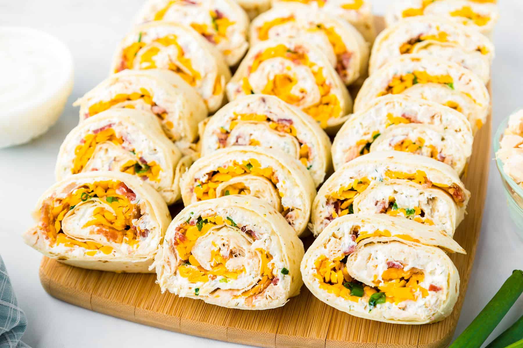 A close-up of chicken bacon ranch pinwheels filled with cheese, herbs, and a creamy spread, neatly arranged on a wooden board.