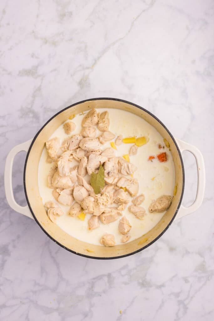 A white pot full of chicken pieces, vegetables and cream for a creamy chicken stew.